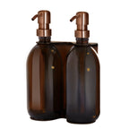 Two brown bottles with copper pumps in a holder on a white background