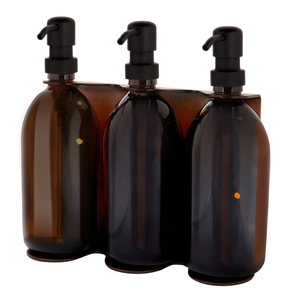 Three amber glass bottles with black pumps in a display stand on a white background