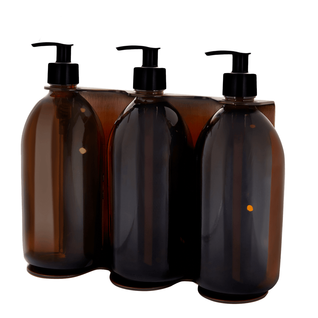 Four amber glass bottles with black pumps in a clear packaging holder on a white background