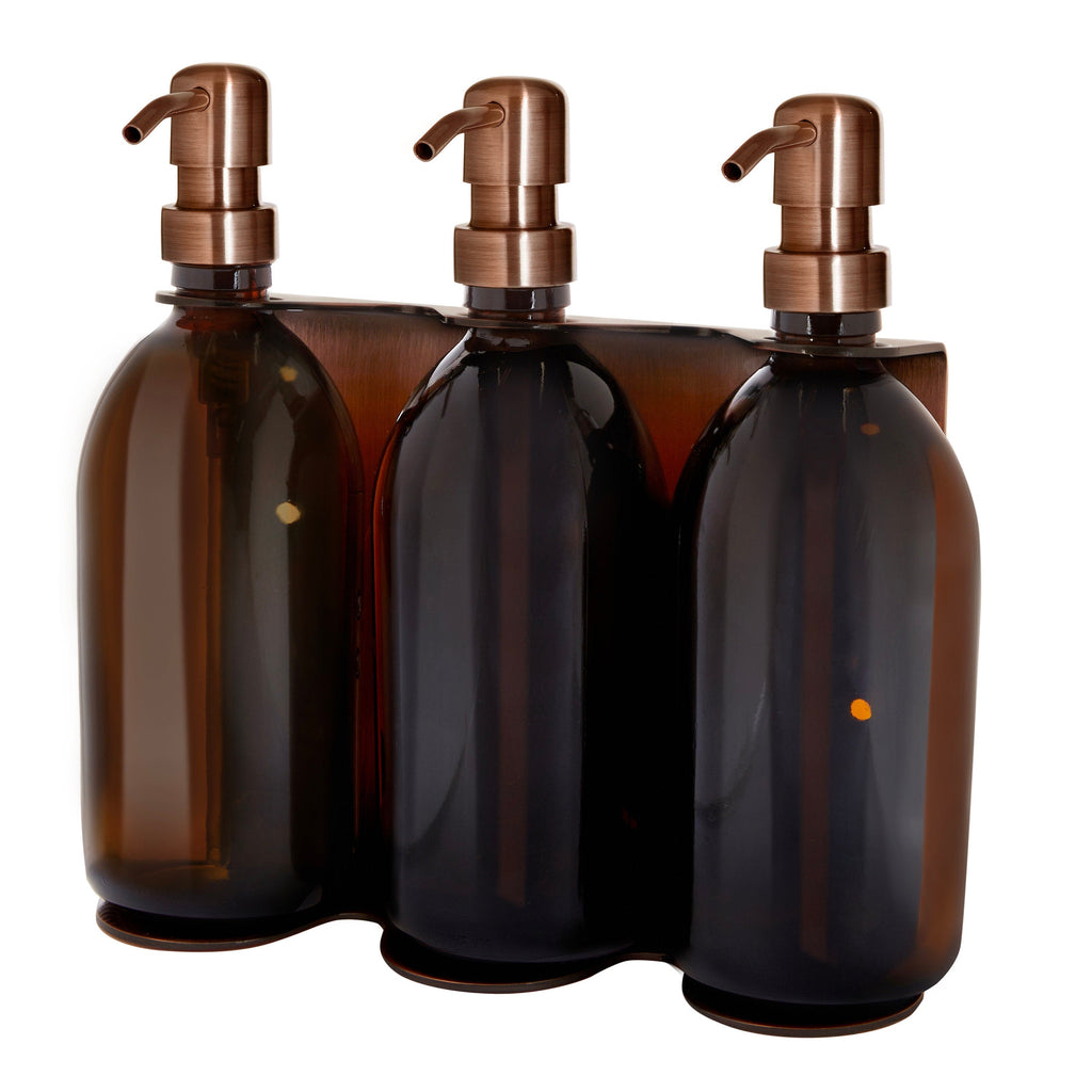 Three amber glass bottles with bronze pumps in a row on a white background