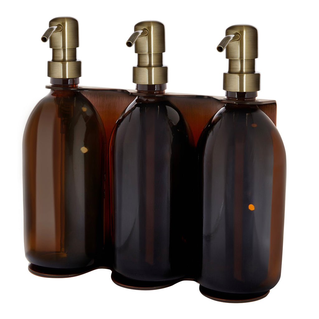 Three amber glass bottles with gold pumps in a wooden holder on a white background