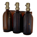 Three amber glass bottles with gold pumps in a wooden holder on a white background