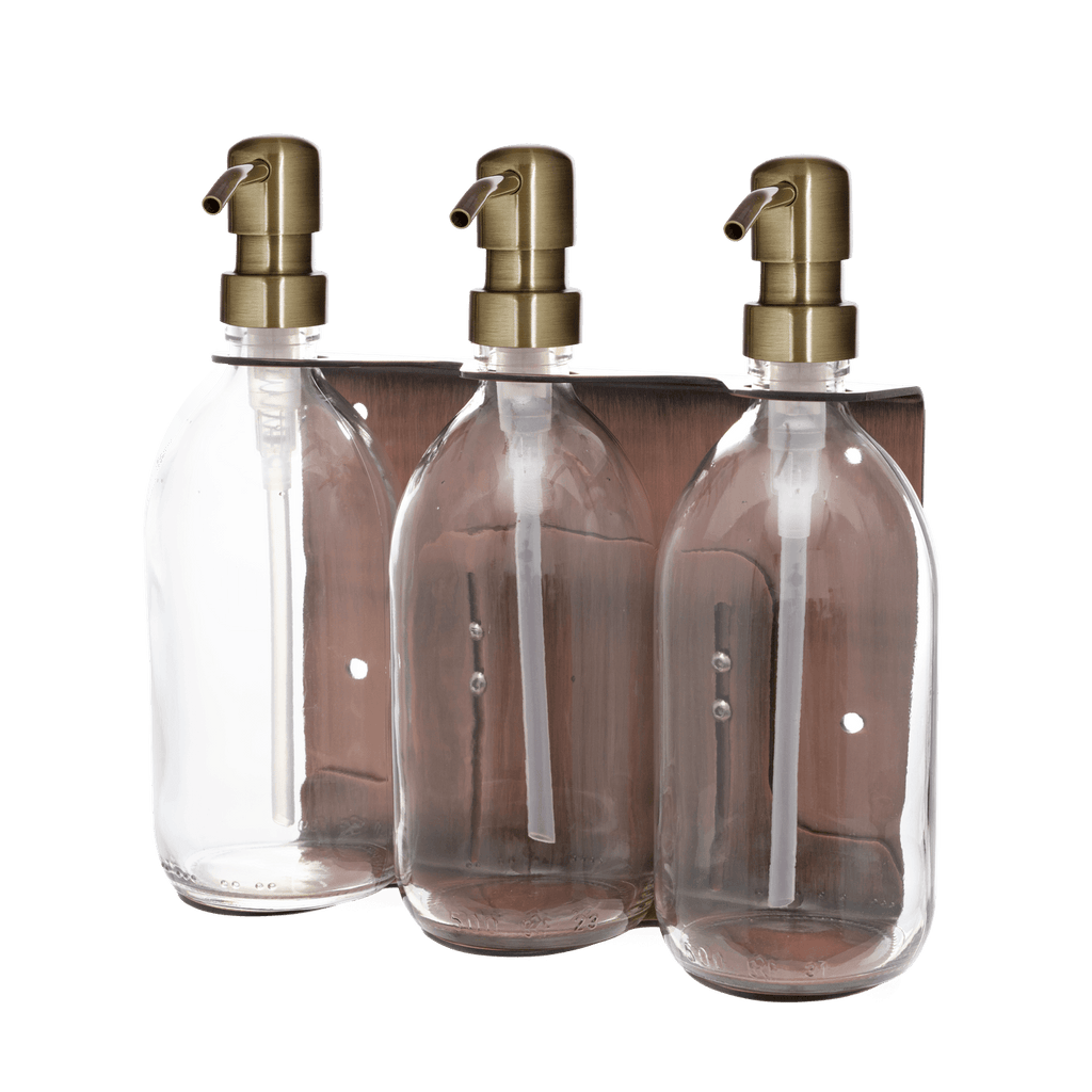 Three clear bottles with gold pumps in a metallic holder on a gradient background
