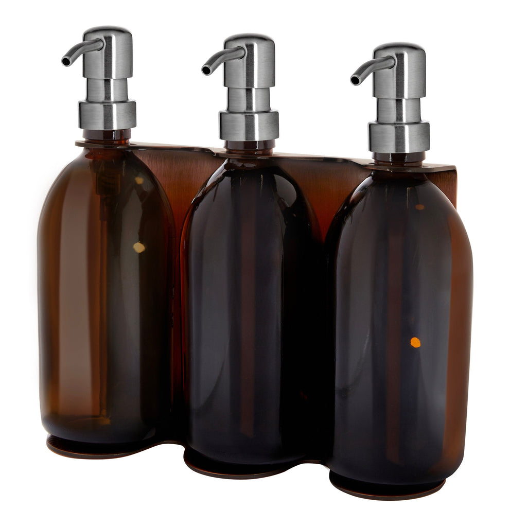 Three amber glass bottles with silver pumps in a wooden holder on a white background