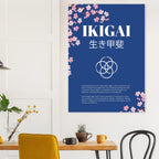 Wall poster titled “IKIGAI” with Japanese characters beneath, featuring cherry blossom illustrations on a deep blue background, displayed in a minimalist interior above a wooden table with plants and mugs.