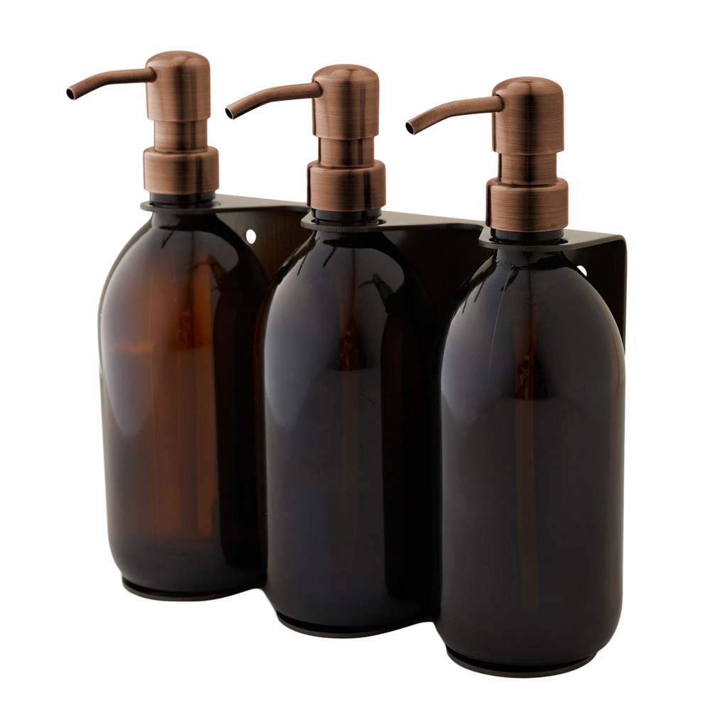 Three brown glass bottles with bronze pumps in a black holder on a white background