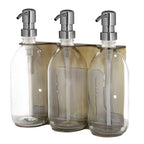 Set of three clear glass bottles with silver pumps in a wooden holder on a white background