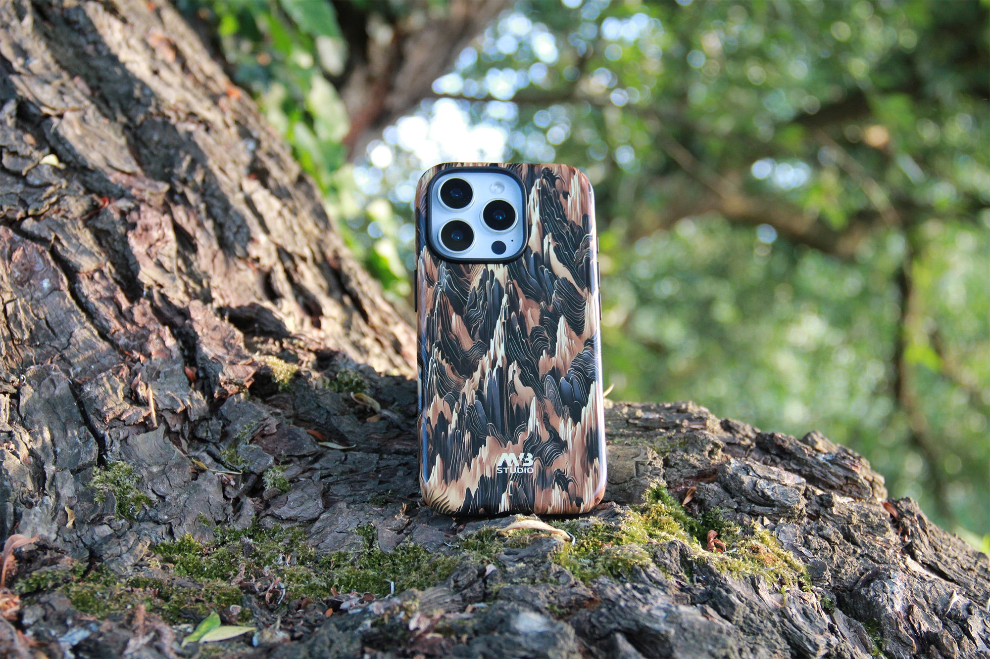 A phone case with a brown and black feather pattern, shown on a smartphone standing on a mossy tree trunk in an outdoor forest setting. Photograph by MVB STUDIO official store.