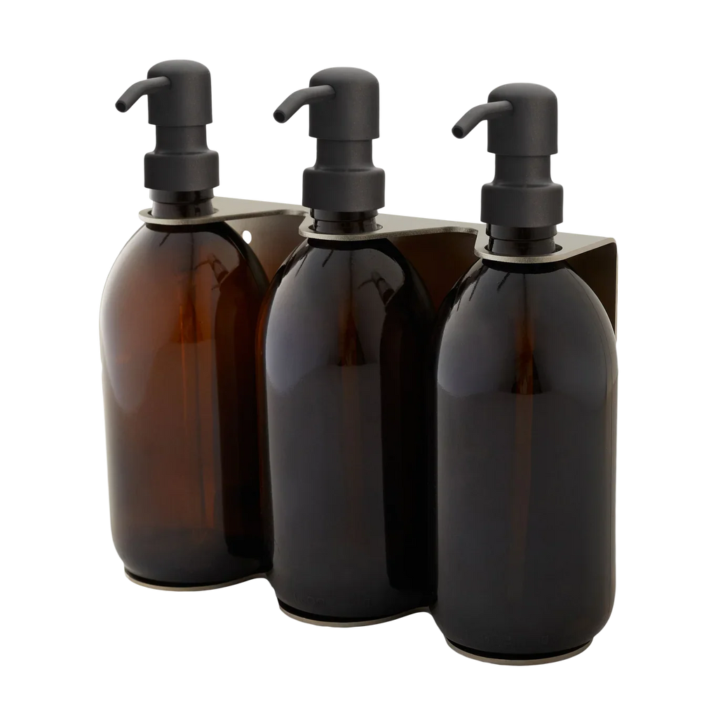 Three amber glass bottles with black pumps in a holder on a white background