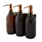 Three dark glass bottles with copper pumps in a holder on a white background