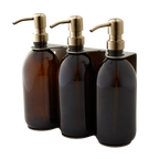 Three amber glass bottles with gold pumps in a holder on a white background