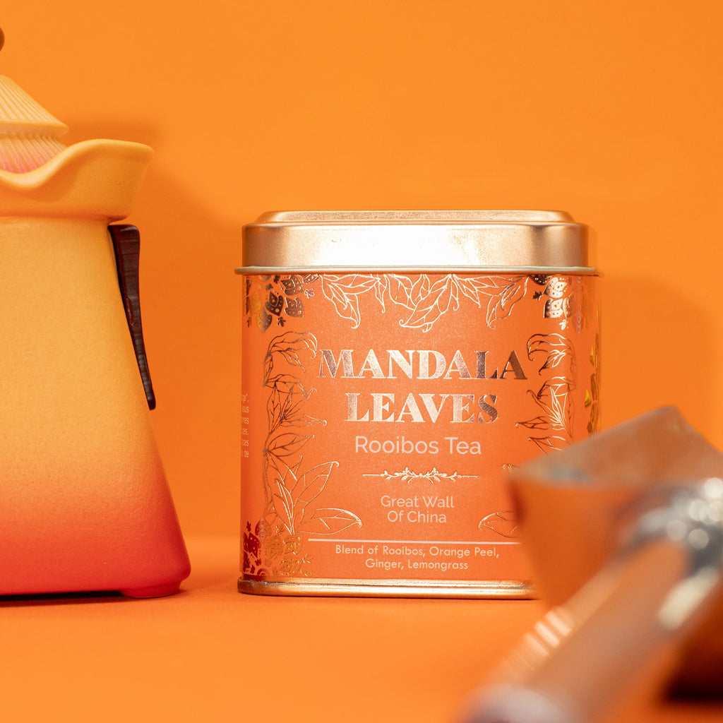 Mandala Leaves Rooibos Tea canister on an orange background with a teapot and cup.