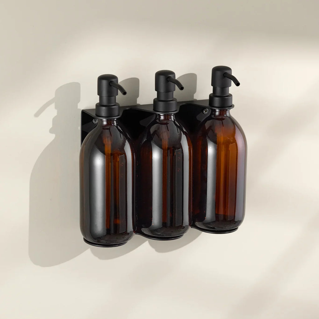 Three amber glass bottles with black pumps on a beige wall.