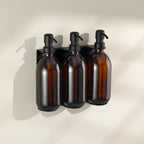 Three amber glass bottles with black pumps on a beige wall.