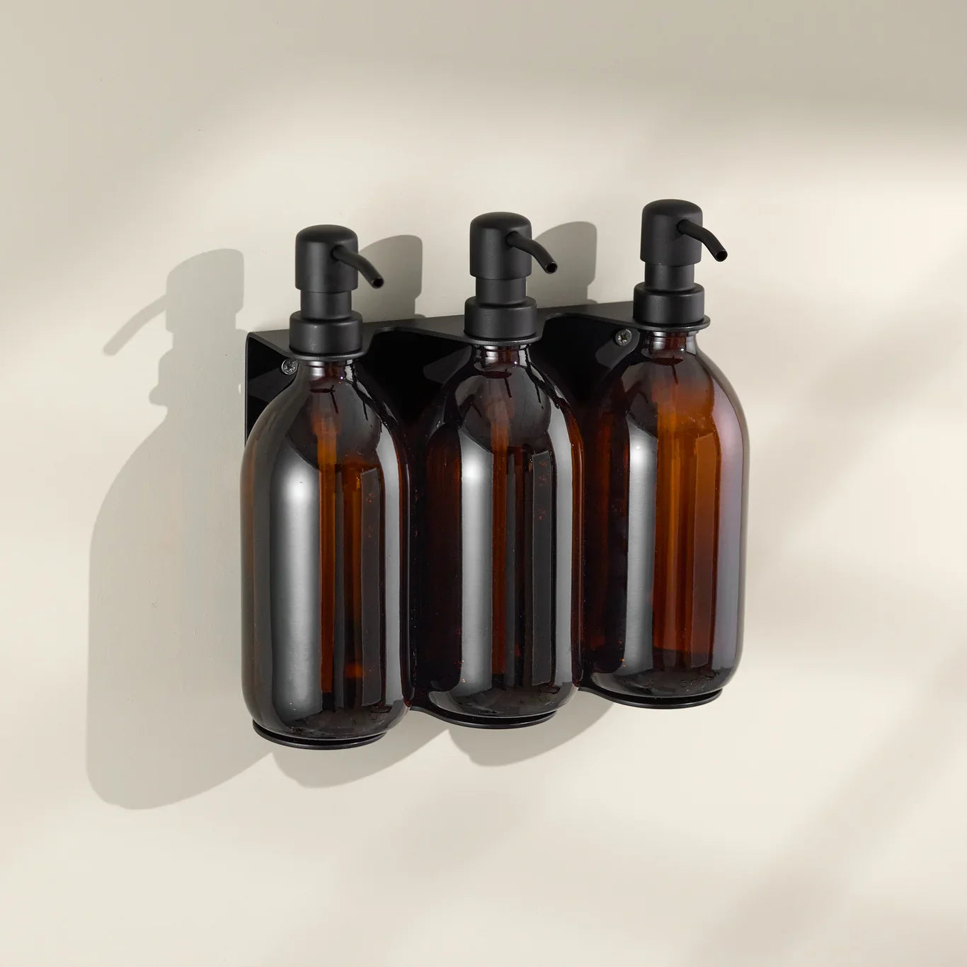 Three amber glass bottles with black pumps on a beige wall.