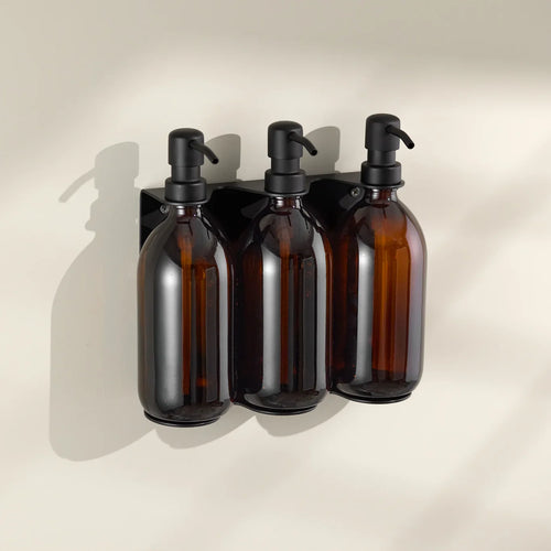 Three amber glass bottles with black pumps on a beige wall.