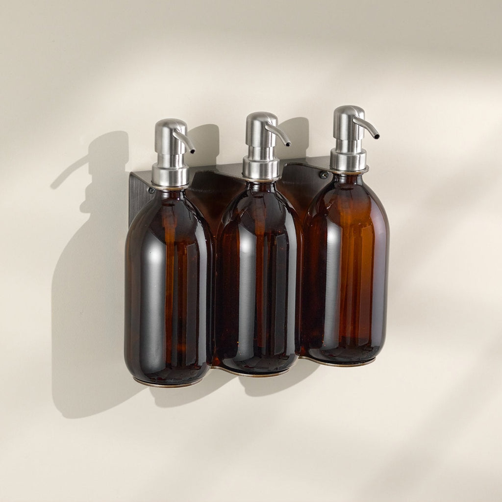 Three brown glass bottles with silver pump dispensers on a beige background